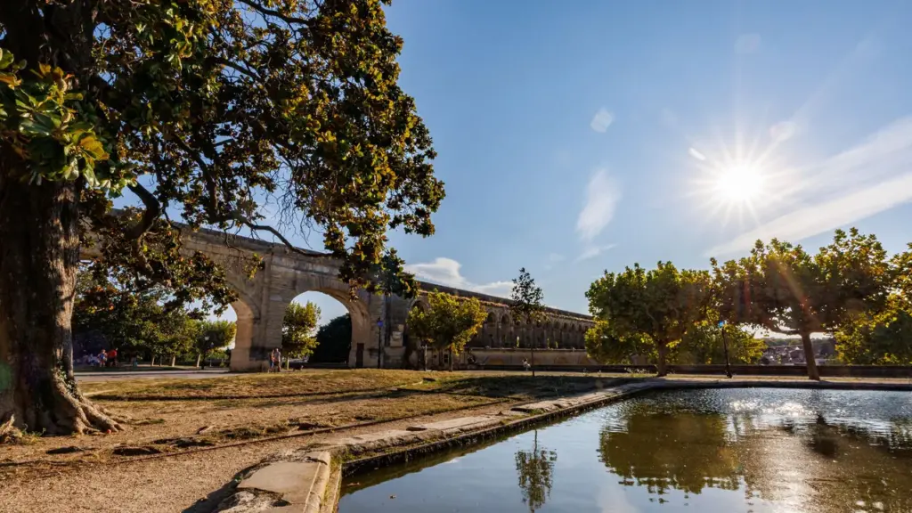 Un ancien aqueduc en pierre dominant un parc ensoleillé avec un petit bassin d'eau.