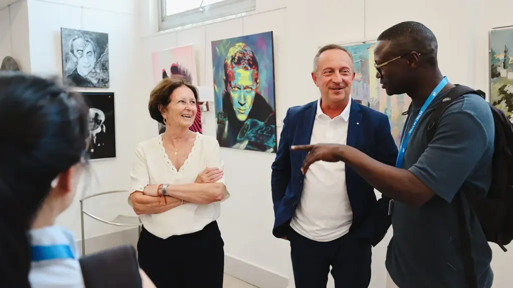 Trois personnes discutent joyeusement dans une galerie d'art entourée de peintures colorées sur les murs.