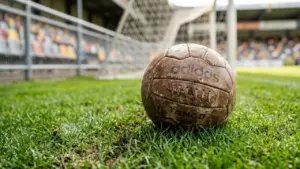 Un vieux ballon de football en cuir usé posé sur l'herbe devant un filet.