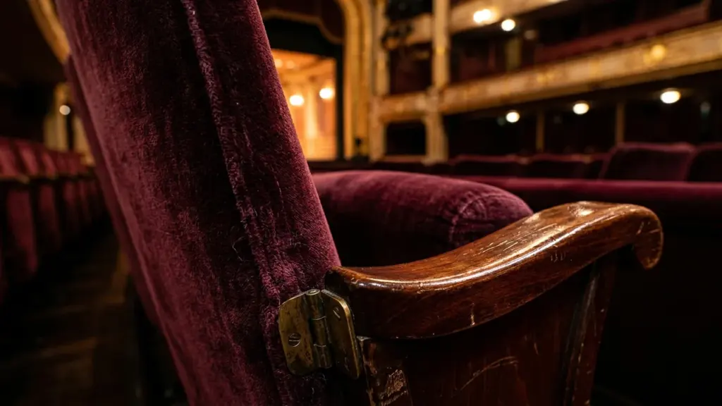 Gros plan sur un fauteuil de théâtre en velours bordeaux avec accoudoir en bois.