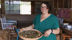 Une femme souriante aux cheveux courts tenant un panier en osier rempli de plantes.