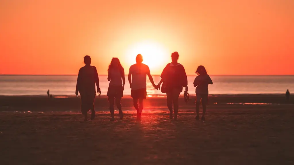 Une famille marchant sur une plage sous un magnifique coucher de soleil orange.