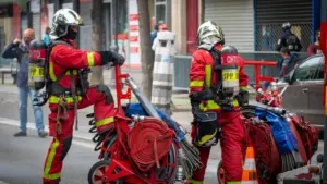 Deux pompiers en tenue d'intervention manipulant du matériel sur la voie publique.