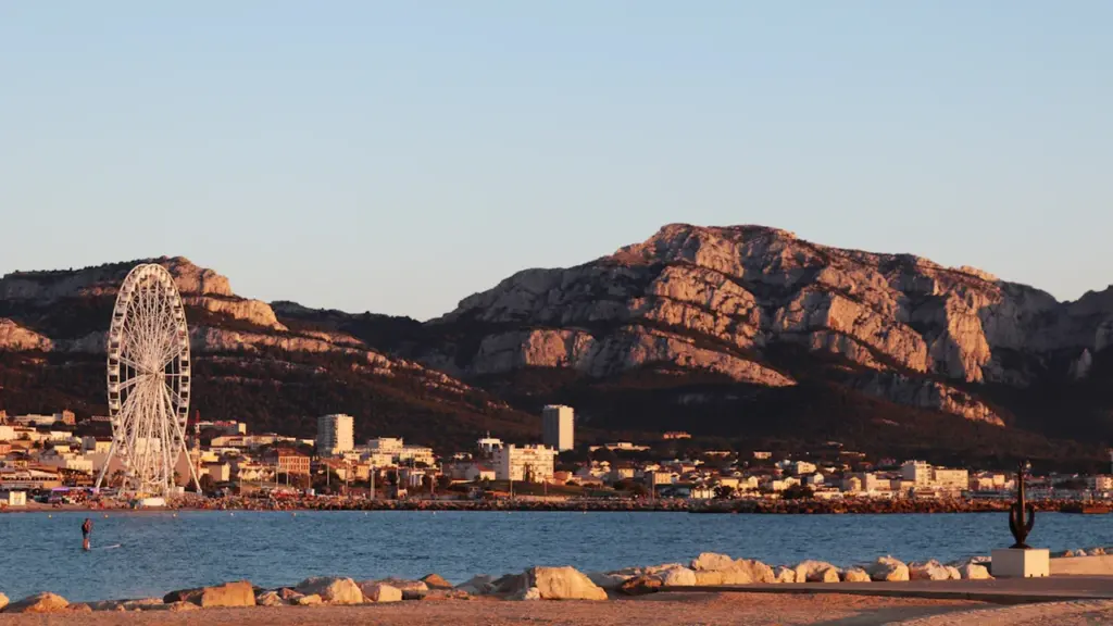 Vue panoramique de la côte marseillaise avec une grande roue et des montagnes rocheuses.