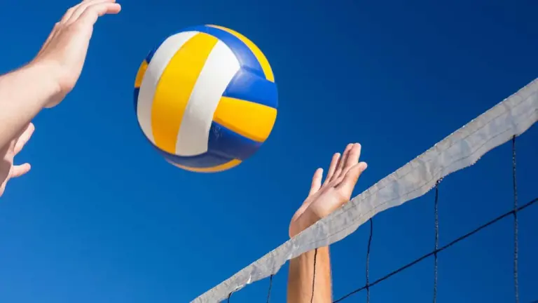 Mains de joueurs de volley-ball s'élevant vers un ballon tricolore sous un ciel bleu.