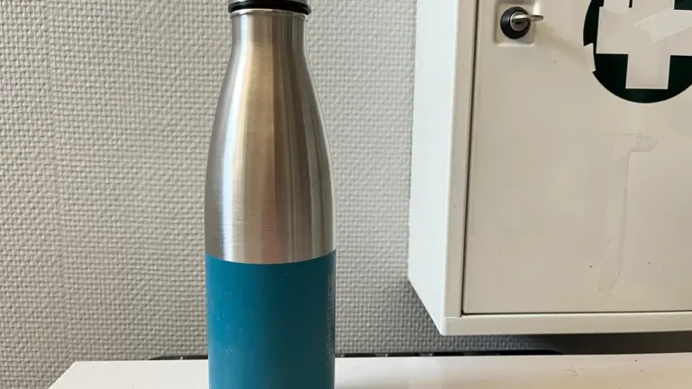 Une bouteille réutilisable en acier inoxydable brossé avec une base bleue posée sur une étagère.