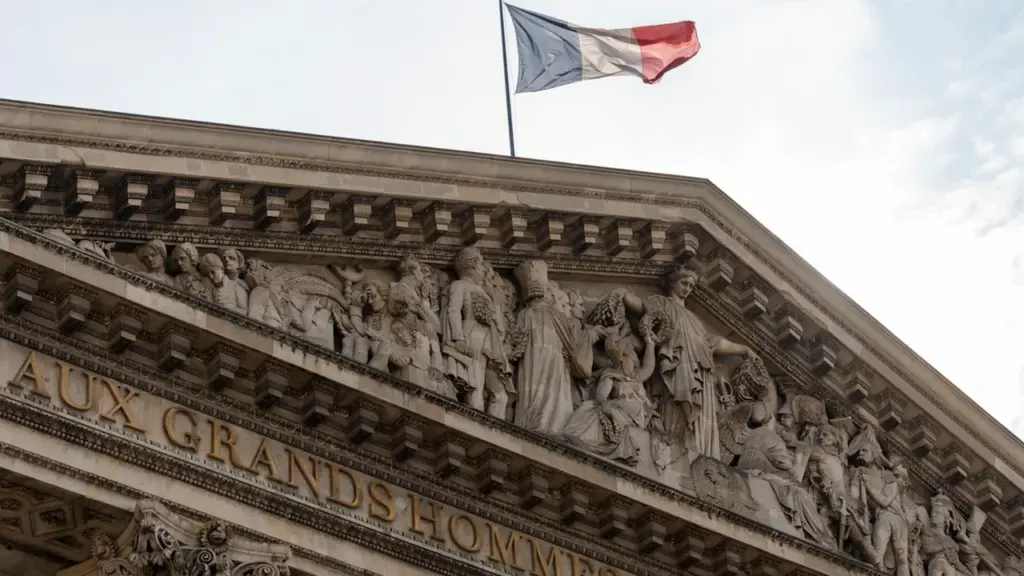 Le drapeau français flotte fièrement au sommet d'un bâtiment historique détaillé sous un ciel bleu.