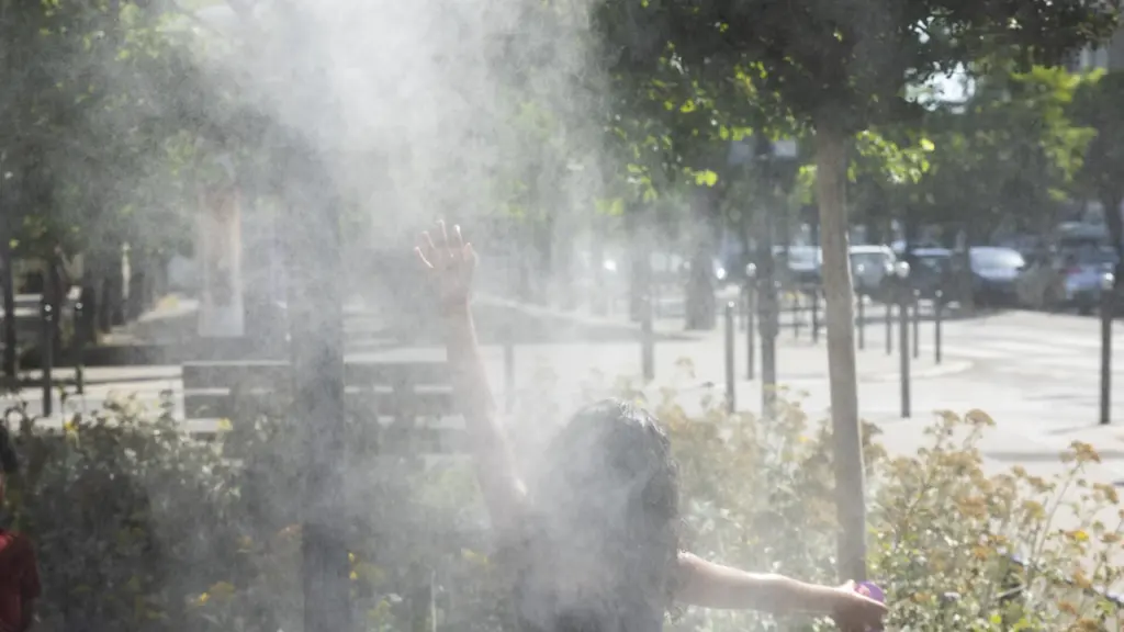 Une personne de dos, bras levés, se rafraîchit sous un jet d'eau brumisateur urbain.