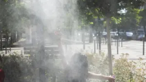 Une personne de dos, bras levés, se rafraîchit sous un jet d'eau brumisateur urbain.