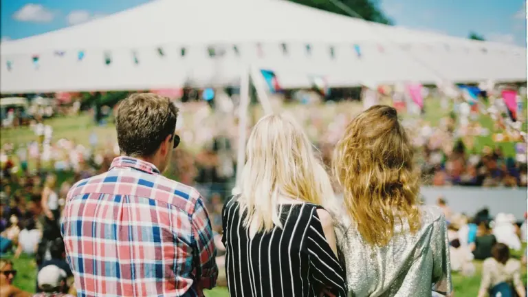 Trois jeunes personnes regardant un festival en plein air depuis une colline herbeuse.