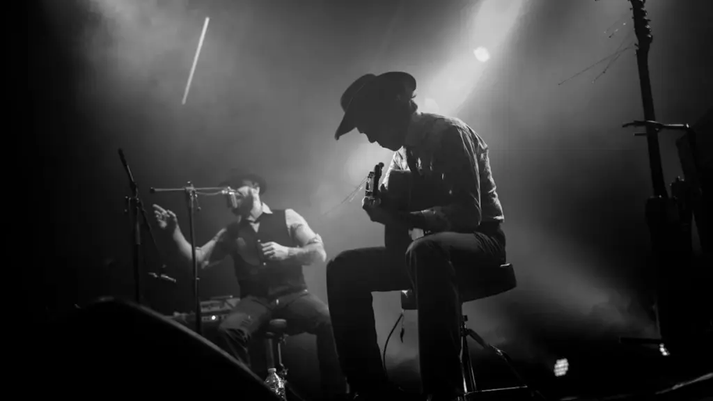 Deux musiciens interprètent un concert acoustique sur scène sous des éclairages tamisés.