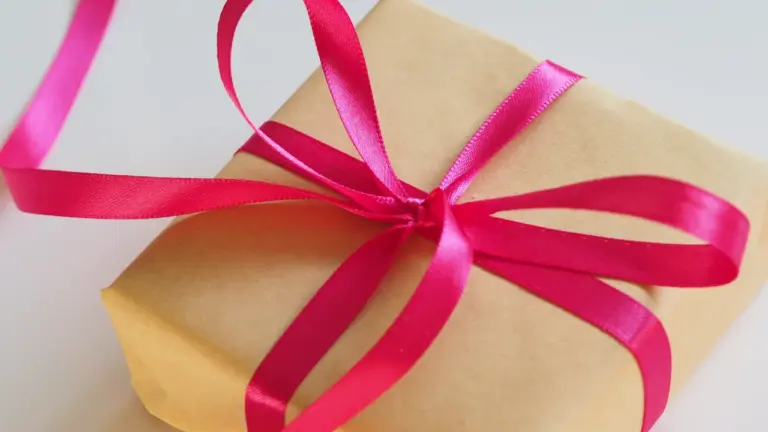 Un petit cadeau emballé dans du papier kraft avec un ruban rose vif.
