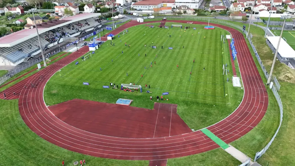 Vue aérienne d'un stade d'athlétisme avec des sportifs sur la pelouse et la piste.