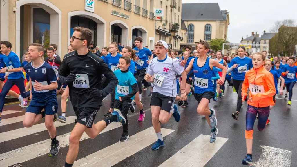 Un groupe de jeunes coureurs avec des dossards participe à une course sur route urbaine.