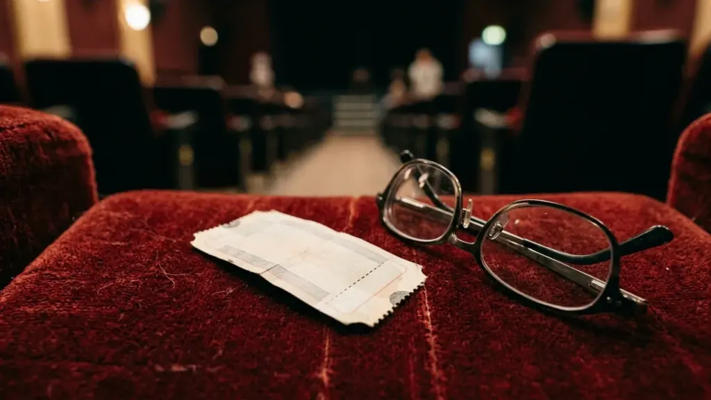 Une paire de lunettes et un ticket de cinéma sur un fauteuil rouge flou.
