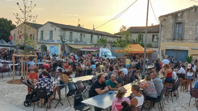 Une foule de personnes dîne sur des tables en plein air lors d'une soirée estivale.