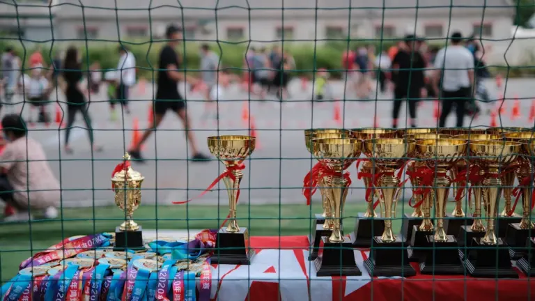 Trophées dorés alignés derrière un filet sur un terrain de sport extérieur.