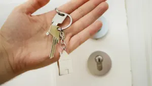 Une main tenant des clés avec un porte-clé en forme de maison devant une porte.