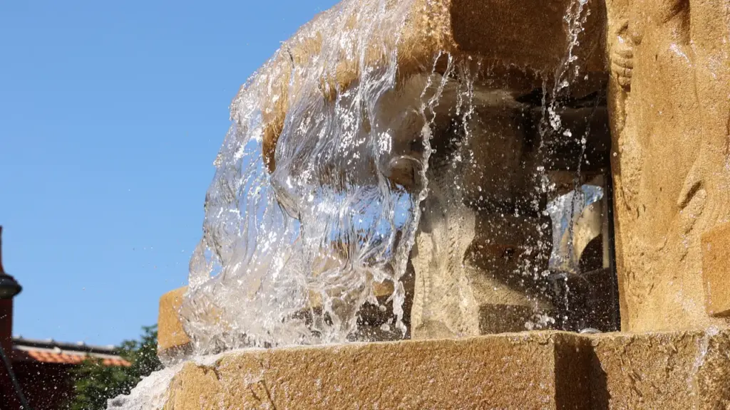 Eau cristalline ruisselant sur une fontaine en pierre dorée sous un ciel bleu dégagé.