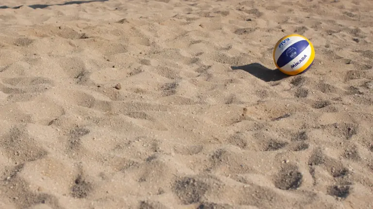 Un ballon de beach-volley posé sur le sable d'un terrain sportif en été.