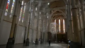 Deux sculptures en grillage métallique suspendues dans une église aux vitraux colorés et colonnes.