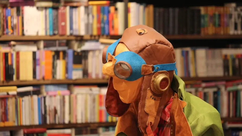Une peluche portant des lunettes d'aviateur devant des étagères de bibliothèque.