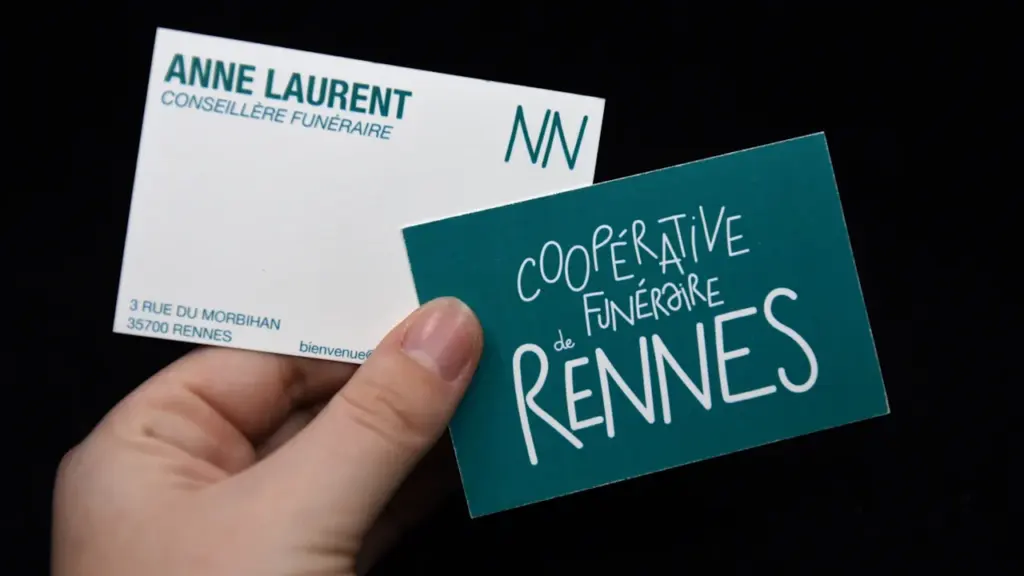 Une main tenant des cartes de visite de la Coopérative Funéraire de Rennes.