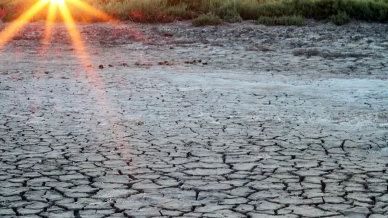 Un sol aride et craquelé sous un soleil couchant brillant à l'horizon d'un paysage.