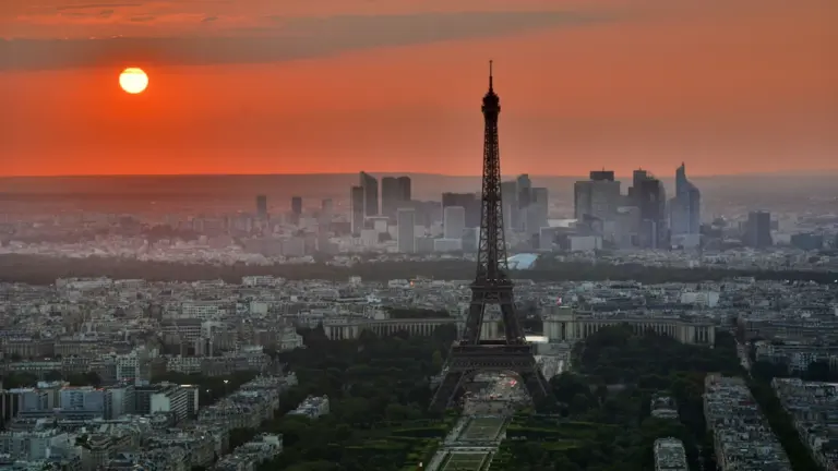 Vue panoramique de la tour Eiffel sous un soleil couchant orangé intense.