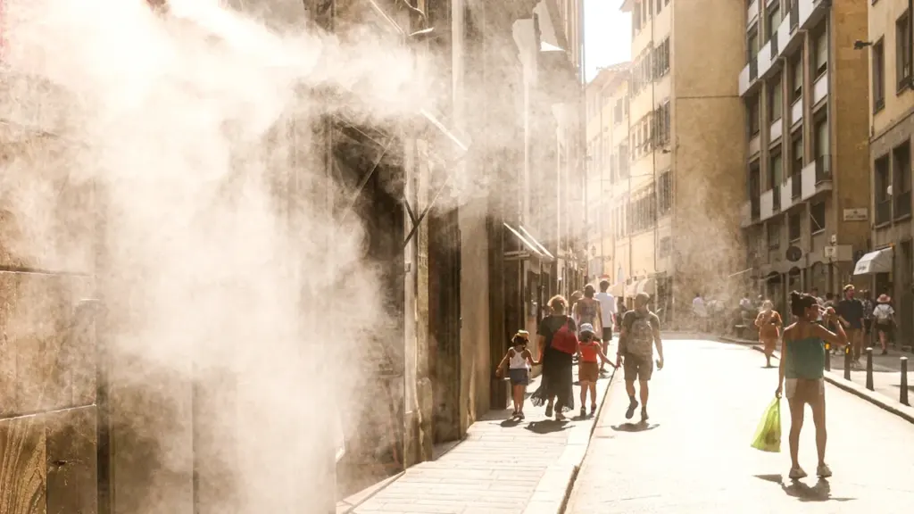 Passants marchant dans une rue ensoleillée sous une brume rafraîchissante pendant la canicule estivale.