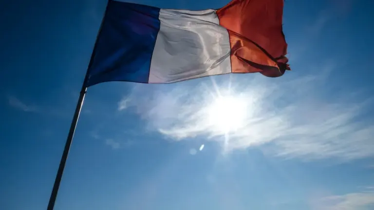 Drapeau français flottant dans un ciel bleu ensoleillé et lumineux.