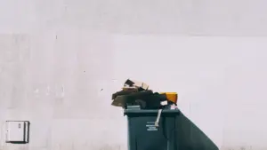 Un bac à ordures noir sur roues placé devant un mur en béton.