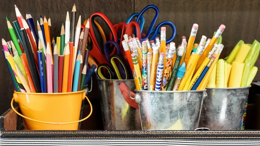 Crayons, ciseaux et fournitures scolaires organisés dans des seaux colorés sur un bureau.