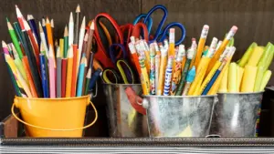 Crayons, ciseaux et fournitures scolaires organisés dans des seaux colorés sur un bureau.