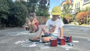 Trois jeunes enfants s'amusent à dessiner des motifs colorés à la craie sur le sol.