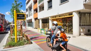 Famille à vélo devant une école avec aménagements urbains modernes et sécurisés.