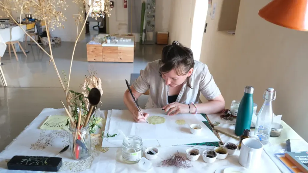 Une femme dessine à la plume sur du papier dans un atelier artistique lumineux.