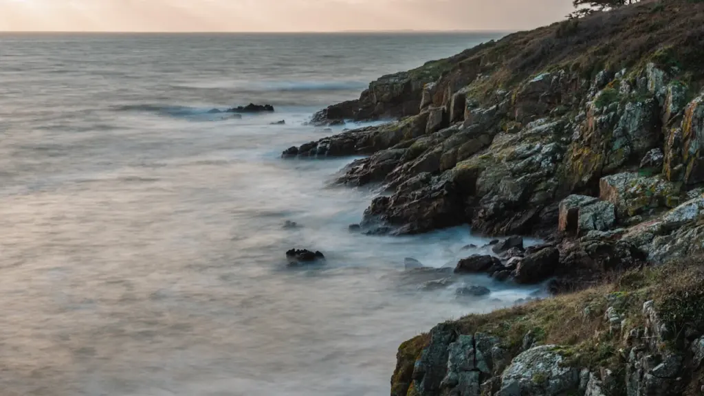 Vagues s'écrasant sur les falaises rocheuses de la côte bretonne sous une lumière douce.