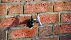 Robinet extérieur en métal fixé sur un mur en briques rouges.