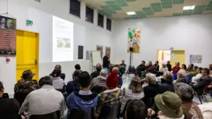 Un groupe de personnes assises assiste à une présentation publique dans une salle communale.