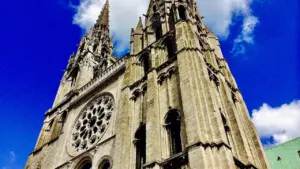 Vue en contre-plongée des flèches emblématiques de la cathédrale de Chartres sous un ciel bleu.