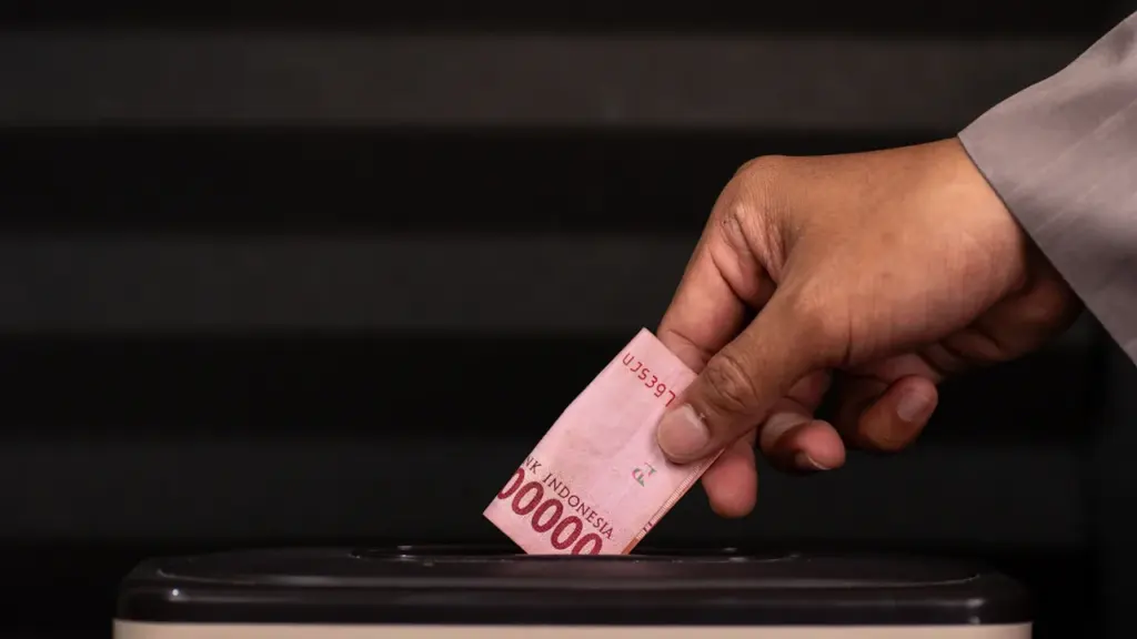Une main insère un don financier dans une urne pour la solidarité.
