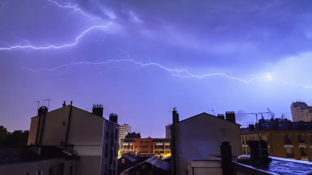 Foudre frappant le ciel au-dessus des immeubles parisiens lors d'un orage nocturne intense.