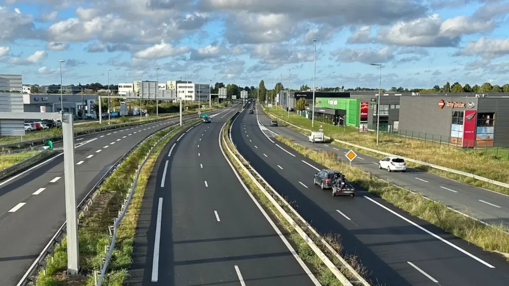 Vue plongeante sur une autoroute à plusieurs voies entourée de bâtiments commerciaux et d'herbes.