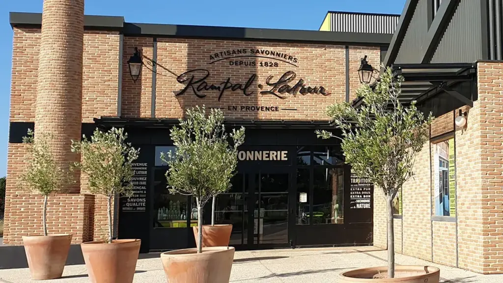 Façade en briques de la savonnerie Rampal Latour avec oliviers en pots devant l'entrée.