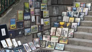 De nombreuses peintures encadrées exposées artistiquement sur des marches en pierre en extérieur.