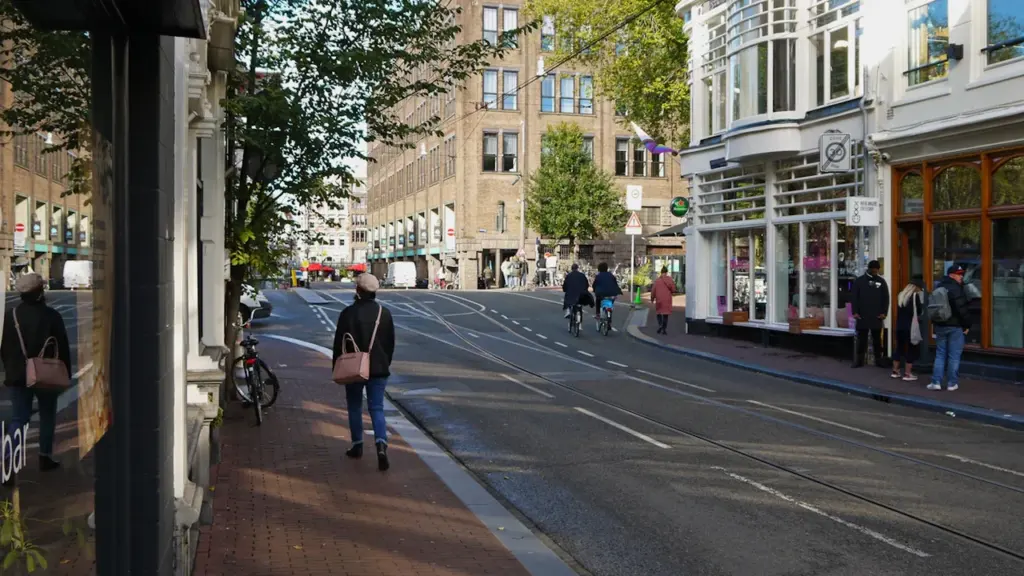 Rue citadine animée avec des piétons, des cyclistes et une architecture européenne classique.
