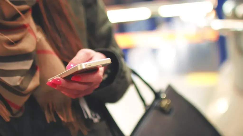Gros plan sur les mains d'une femme utilisant un smartphone avec des ongles vernis rose.