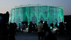 Structure architecturale moderne avec des motifs géométriques illuminés en vert la nuit.