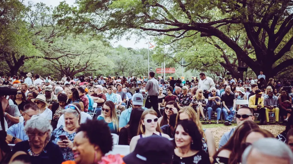 Une foule rassemblée en extérieur pour un événement citoyen sous les grands arbres.